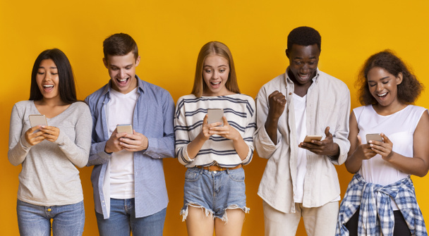 Emotional teen friends staying in row, using mobile phones - Valokuva, kuva