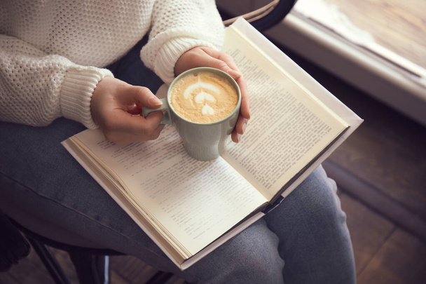 Woman with cup of coffee reading book indoors, closeup - Foto, Imagen