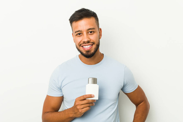 Young south-asian man holding an after shave cream happy, smiling and cheerful. - Photo, image