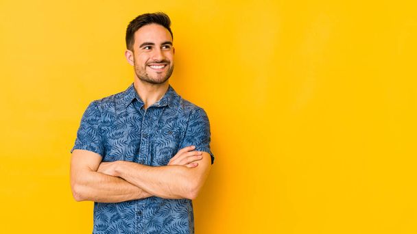 Young caucasian man isolated on yellow bakground smiling confident with crossed arms. - Photo, Image