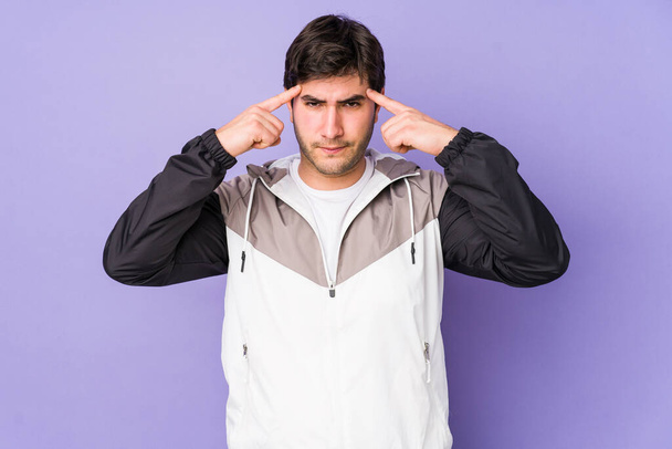 Young man isolated on purple background focused on a task, keeping forefingers pointing head. - Fotografie, Obrázek