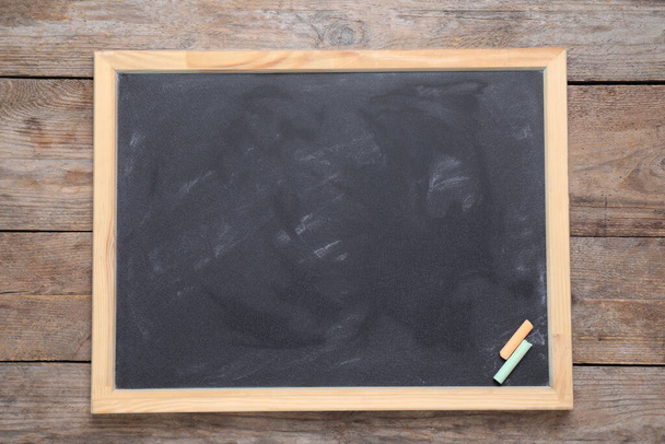 Blackboard with pieces of color chalk on wooden background, top view. Space for text - Photo, Image