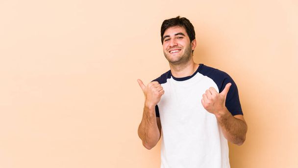 Young man isolated on beige background raising both thumbs up, smiling and confident. - Fotografie, Obrázek