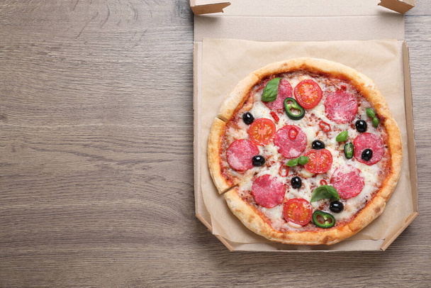 Delicious pizza Diablo in cardboard box on wooden background, top view. Space for text - Foto, afbeelding