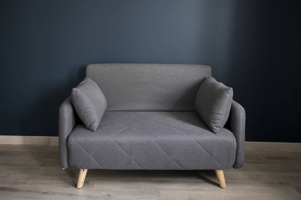 Gray soft sofa with 2 pillows. Modern design sofa on blue background in empty room. Copy space. - Φωτογραφία, εικόνα