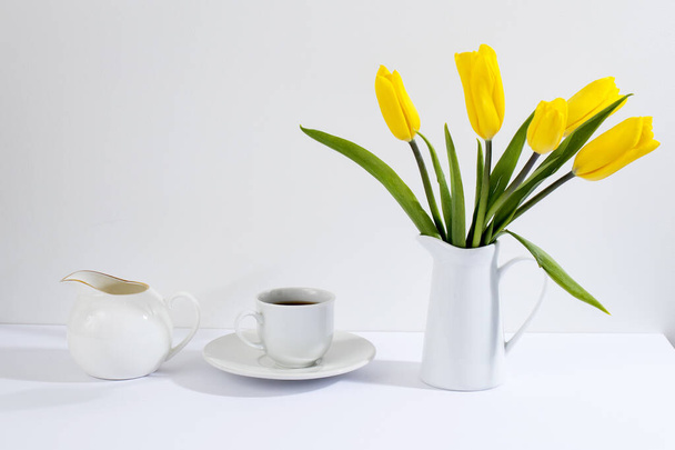 bouquet of yellow tulips is on the table opposite white wall. Copy space - Zdjęcie, obraz