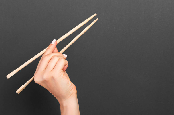 黒い背景に女性の手に木の箸の創造的なイメージ。コピースペース付きの和食と中華料理. - 写真・画像