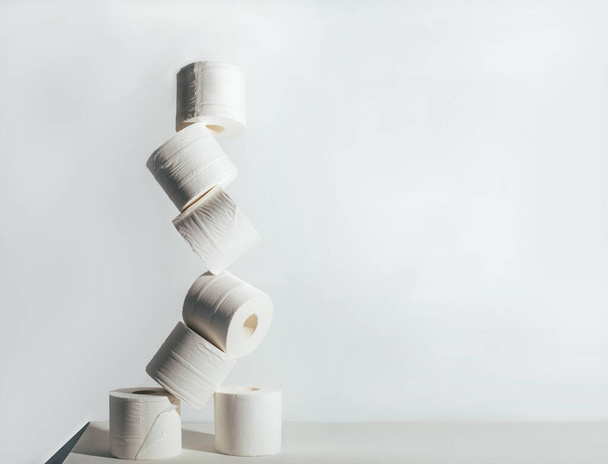 Рулоны туалетной бумаги нестабильно стоят друг на друге на белом фоне
 - Фото, изображение