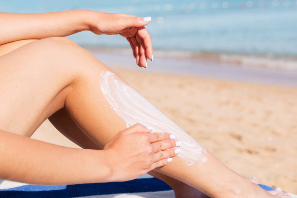 Mujer bonita está aplicando crema solar en su pierna con su mano relajándose en la tumbona junto al mar
. - Foto, Imagen