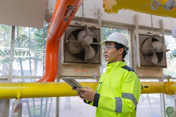 Asian engineer wearing glasses working in the boiler room, maintenance checking technical data of heating system equipment - Valokuva, kuva