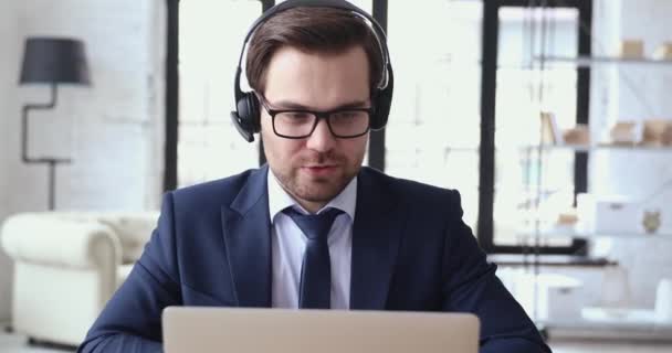Male executive wears headset video calling by webcam on laptop - Felvétel, videó