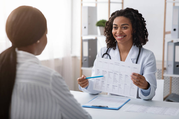 Vrolijke vrouwelijke dietoloog toont patiënt behandelplan tijdens overleg - Foto, afbeelding