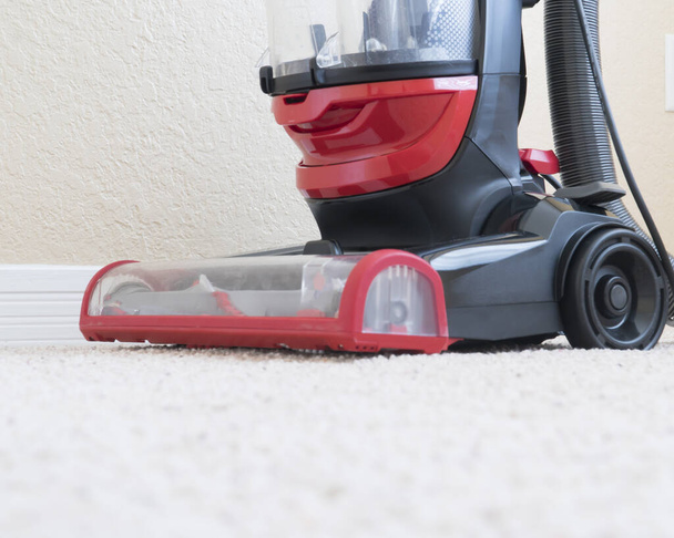 Vacumm cleaner is used to clean a carpet surface while doing houshold chores - Photo, Image