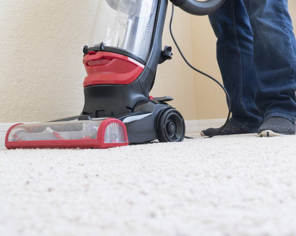 Vacumm cleaner is used to clean a carpet surface while doing houshold chores - Photo, image