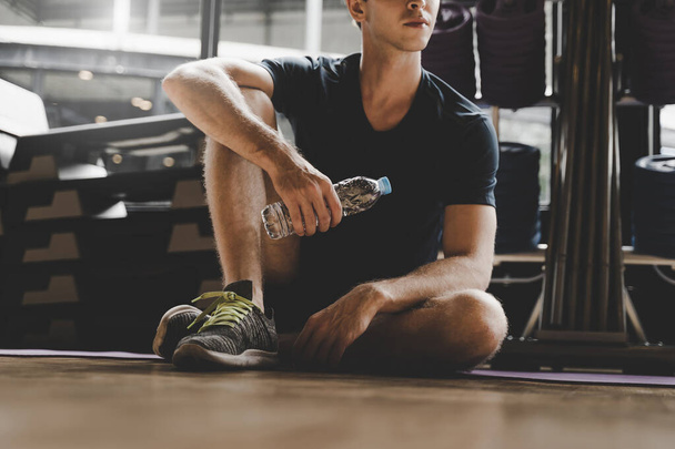muscular caucasian young handsome man taking a break relax and drinking water while resting after workout for good healthy in fitness gym at morning, bodybuilder, lifestyle and sport exercise concept - Foto, Imagem