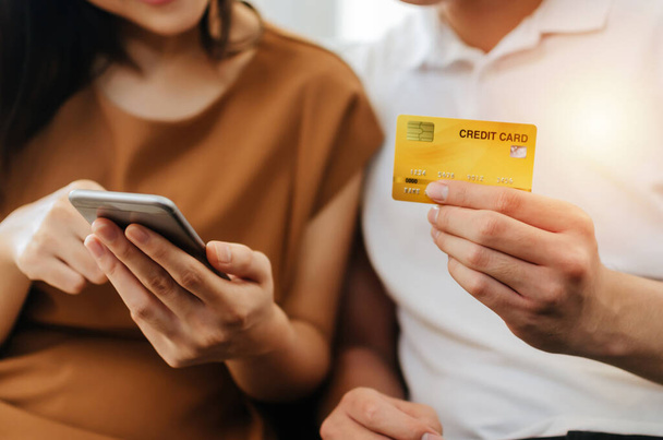 junges asiatisches Paar gibt Sicherheitscode auf dem Handy ein und bezahlt Kreditkarte auf dem Sofa im Home Office, Internettechnologie, elektronische Online-Buchung, Bezahlung und Online-Shopping-Konzept - Foto, Bild