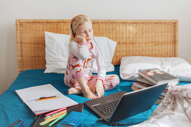 Müde gelangweilte kaukasische Mädchen, die im Bett sitzen und online im Internet lernen. Virtueller Unterricht auf Video während der Selbstisolierung zu Hause. Entfernte Videoerziehung. Moderne Schulstudie für Kinder. - Foto, Bild