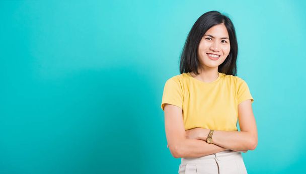 Portrait Asian beautiful young woman standing smile seeing white teeth, She crossed her arms and looking at camera, shoot photo in studio on blue background. copy space to put text on left-hand side. - Fotó, kép