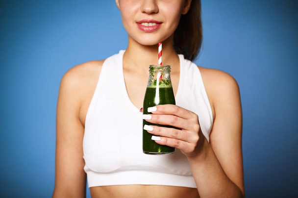Crop delighted young woman with green smoothie laughing against wall background - Foto, immagini