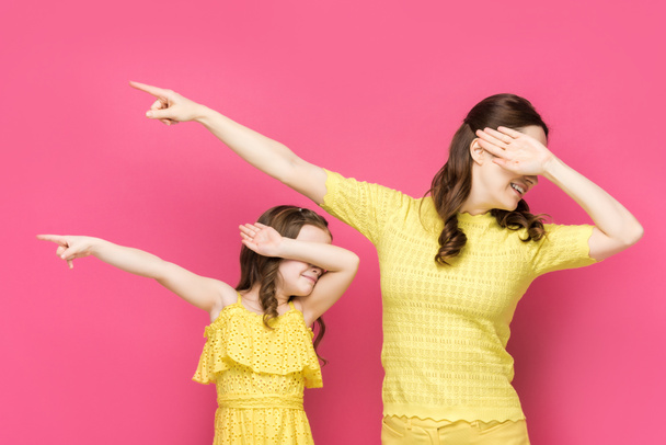 cheerful mother and daughter with obscure faces pointing with fingers away isolated on pink  - Photo, image