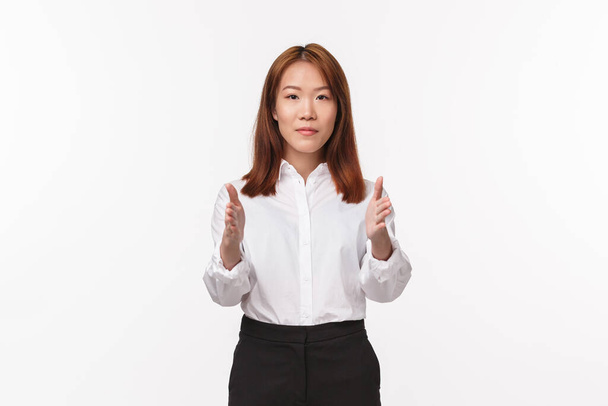 Portret młodej eleganckiej Azjatki w ubraniach biurowych, wskazującej kamerę, pokazującej drogę, instruktorka dająca wskazówki, ucząca nowych stewardess, stojąca na białym tle - Zdjęcie, obraz