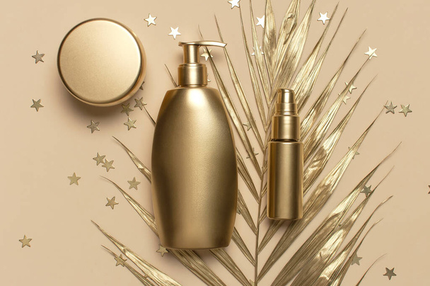Cosmetic mock up gold bottles. Cosmetics Branding Concept. Cosmetic containers, golden tropical palm leaves, stars confetti on beige background. Flat lay top view. Cosmetic products, beauty. - Photo, Image