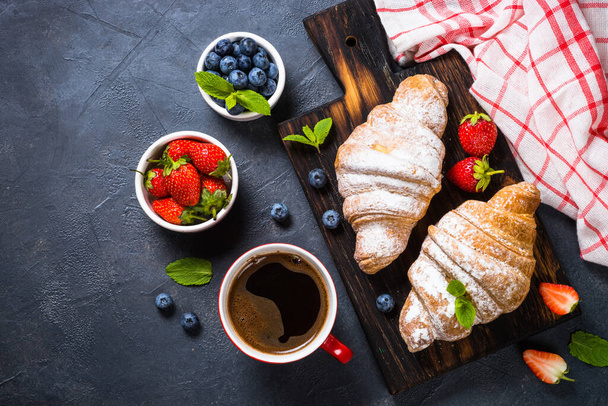 Croissant with fresh berries and cup of coffee on black. - Photo, Image