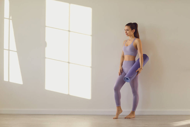 Yoga woman. Happy sport woman with yoga mat on white wall in a bright room. - Фото, зображення