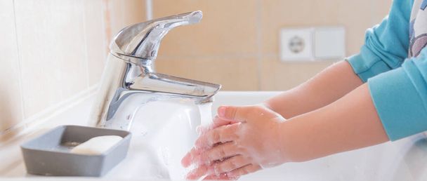Primo piano delle mani saponose di un bambino che vengono lavate sotto l'acqua corrente in un lavandino
 - Foto, immagini
