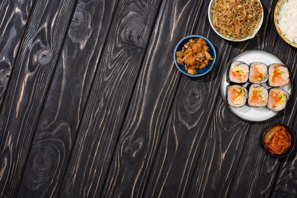 ylhäältä näkymä kulhoja Korean lisukkeet lähellä maukasta riisiä rullina puupinnalla
  - Valokuva, kuva