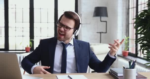 Excited businessman listening music pretending playing guitar in office - Materiał filmowy, wideo