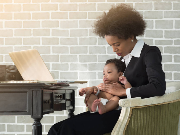 African working at home mother in business suits with infant on the laps. Businesswoman, single mom, feeling worried and trying to comfort sick baby boy. Business, Single mom or Women's day concept. - Foto, immagini