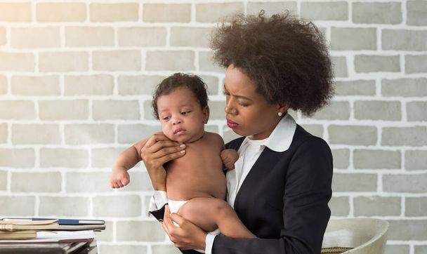 Afrikai anya öltönyben tartja a fiát, miközben otthon dolgozik. Kényelmetlen csecsemő stresszes anyával. Üzleti, egyedülálló anya vagy női nap koncepció. - Fotó, kép
