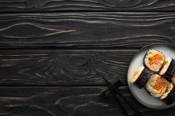 top view of plate with korean gimbap and chopsticks on wooden surface  - Fotó, kép