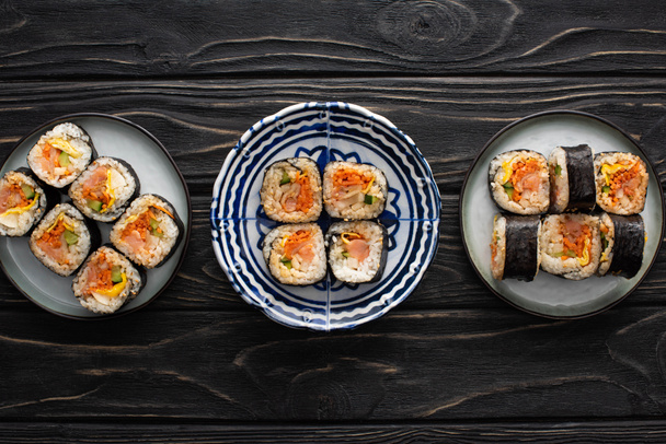 top view of plates with tasty and korean gimbap on wooden surface  - Photo, Image