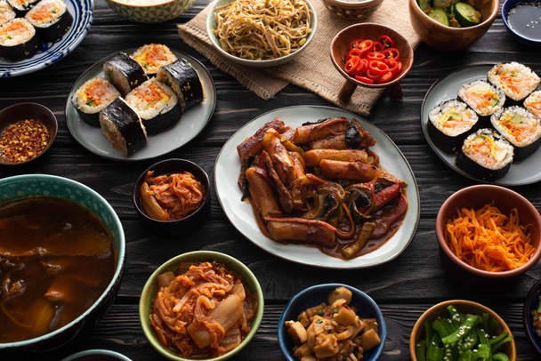 πιάτα και κύπελλα με κορεάτικα πιάτα πλευρά και gimbap σε ξύλινη επιφάνεια  - Φωτογραφία, εικόνα