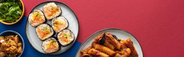 panoramic shot of plates with tasty gimbap near korean side dishes on blue and crimson  - Photo, Image