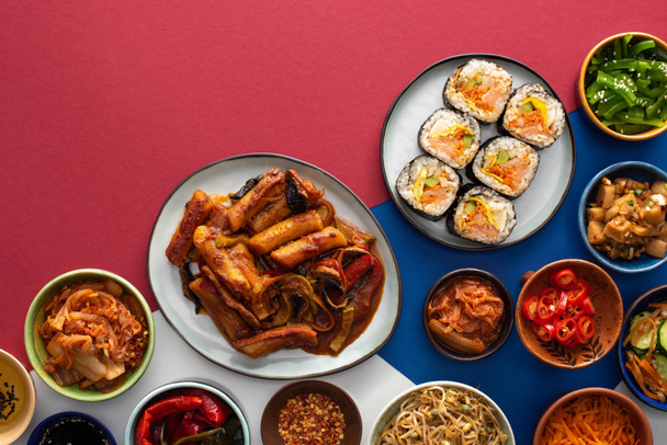top view of fresh gimbap near korean side dishes on white, blue and crimson  - Fotó, kép