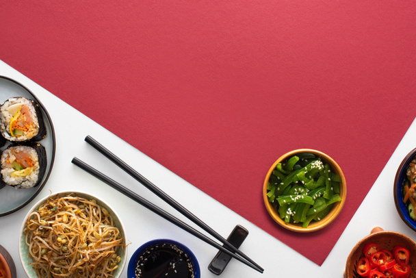 κορυφαία άποψη του φρέσκου κορεατικού gimbap και πλευρικά πιάτα κοντά chopsticks σε λευκό και κόκκινο  - Φωτογραφία, εικόνα
