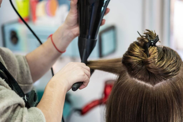 A closeup shot of a hairdresser blow drying a woman's short hair in a beauty salon - Фото, зображення
