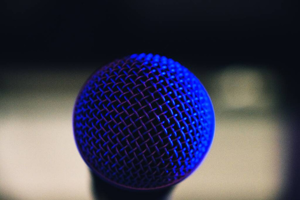 A selective focus shot of a microphone net reflecting blue light from the stage - Foto, imagen