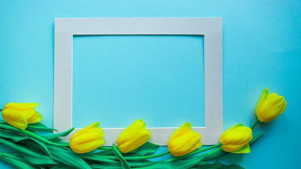 Feliz cartão de primavera. Cartão de saudação criativo com o buquê de belas flores de tulipas amarelas da primavera no fundo azul claro. Copiar espaço, banner ou modelo. Flat lay, natureza morta, vista superior
. - Foto, Imagem