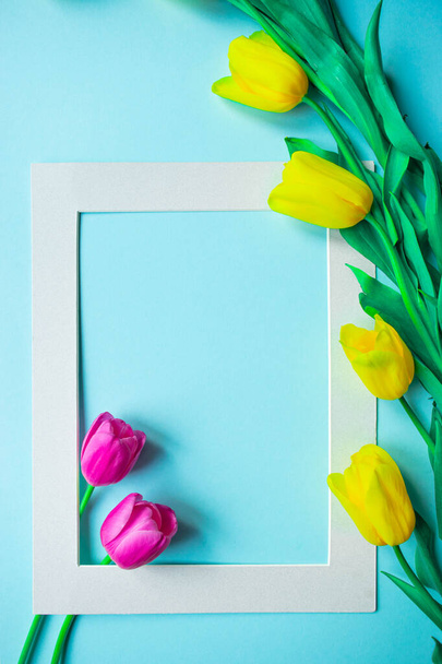 幸せな春のカード。ライトブルーの背景に美しい春の黄色のチューリップの花の花束と創造的なグリーティングカード。スペース、バナー、またはテンプレートをコピーします。フラットレイアウト、静物画、トップビュー. - 写真・画像