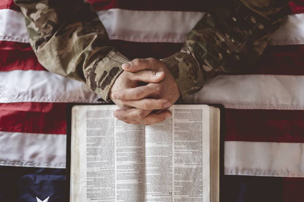 Un soldato americano piange e prega con la bandiera americana e la Bibbia davanti a lui
 - Foto, immagini
