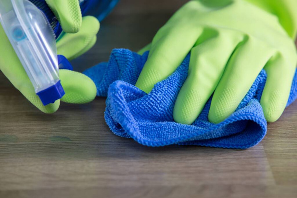 Egy szobalány gumikesztyűvel tisztítja az asztalt egy mikroszálas tisztító ruhával és sterilizáló spray palackkal. - Fotó, kép