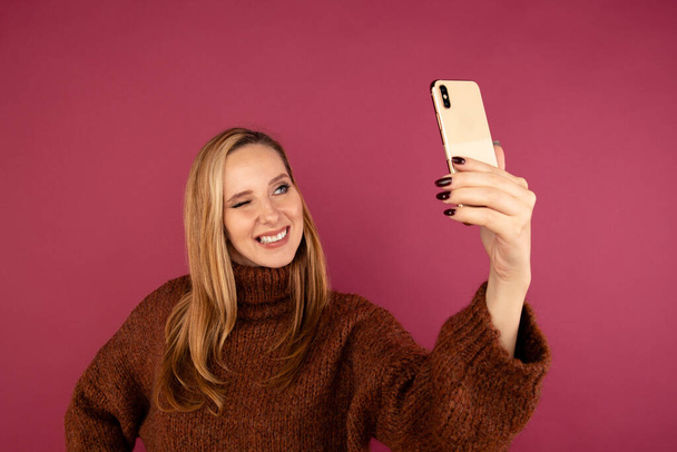 Jovem senhora em suéter fazendo auto foto no telefone no estúdio rosa
. - Foto, Imagem