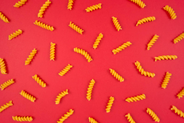 Spirals pattern on red background. Italian food. Pasta composition. Flat lay layout. - Photo, Image