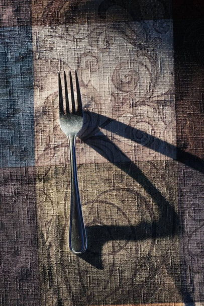 A vertical high angle closeup shot of a fork utensil on a tablecloth under the dramatic light - Foto, Imagen
