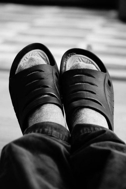 Μια κάθετη γκρι κλίμακα υψηλής γωνίας κοντινό πλάνο των ανθρώπινων ποδιών σε μαύρες παντόφλες - Φωτογραφία, εικόνα