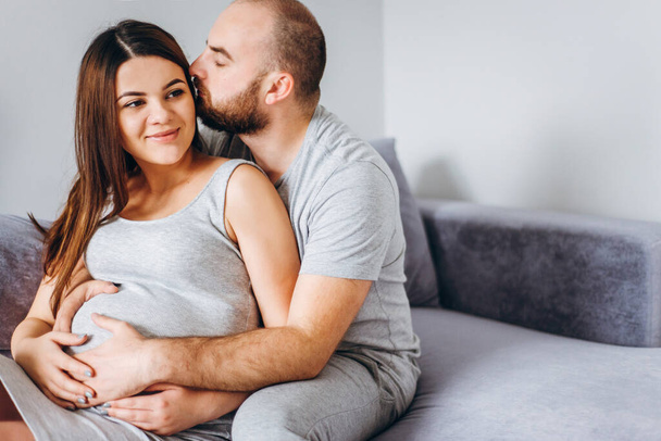 Terhesség. Fiatal pár várja a babát. Csodálatos várandós szülők ölelkeznek a lakásukban, várva a szülést. - Fotó, kép